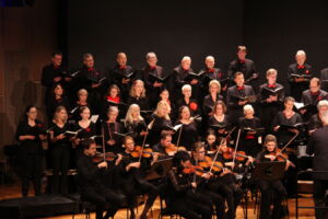A choir performing on stage with a group of musicians playing string instruments in front.