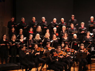 A choir performing on stage with a group of musicians playing string instruments in front.