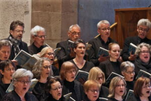 A choir dressed in black performs in a church, holding sheet music and singing with concentration and emotion.