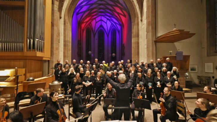 A choir and orchestra perform in a grand cathedral with colorful lighting illuminating the arched ceiling.