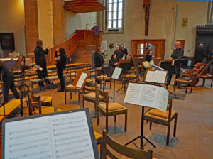 Musicians setting up in a church-like venue with music stands and seating arranged.