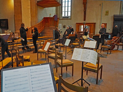 Musicians setting up in a church-like venue with music stands and seating arranged.