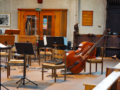 Empty orchestra stage with scattered chairs, music stands, and a double bass leaning against a chair.