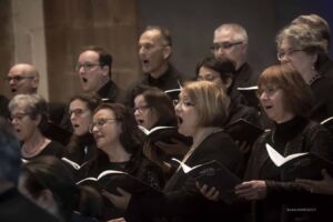 A choir of adults singing passionately, each holding a music book.