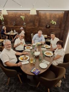 Five people sitting around a round table at a restaurant, enjoying a meal with drinks and smiling.